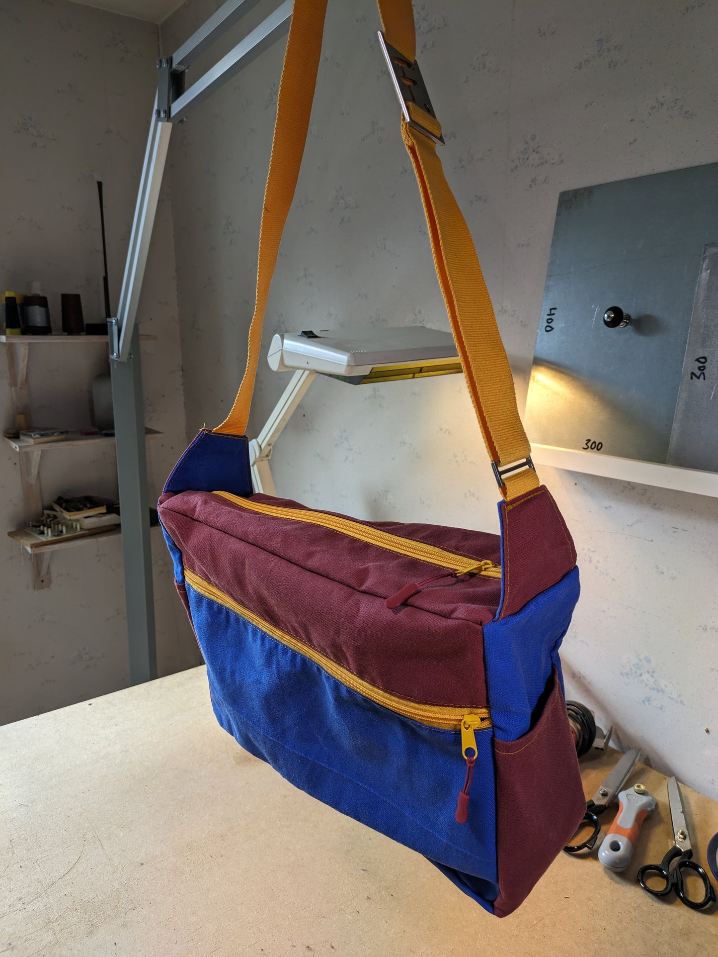 Shoulder bag in burgundy and blue with yellow zippers and strap