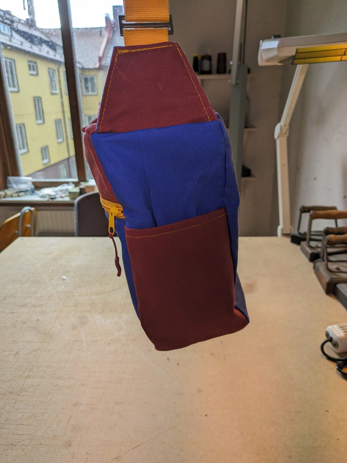 Shoulder bag in burgundy and blue with yellow zippers and strap