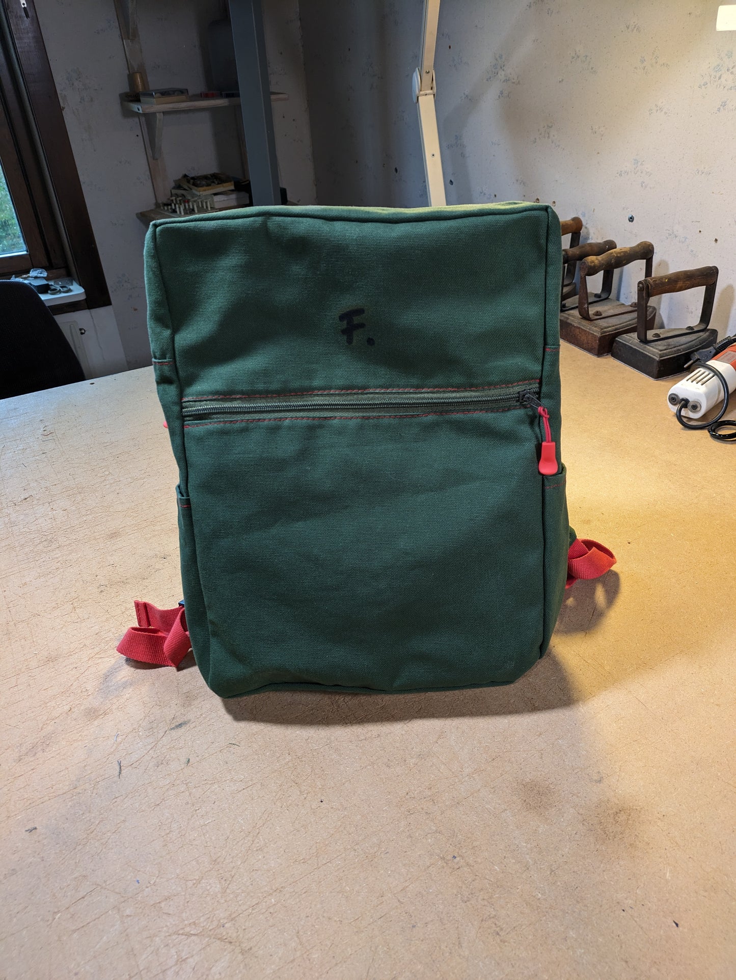 Green backpack with green zippers, red thread and straps