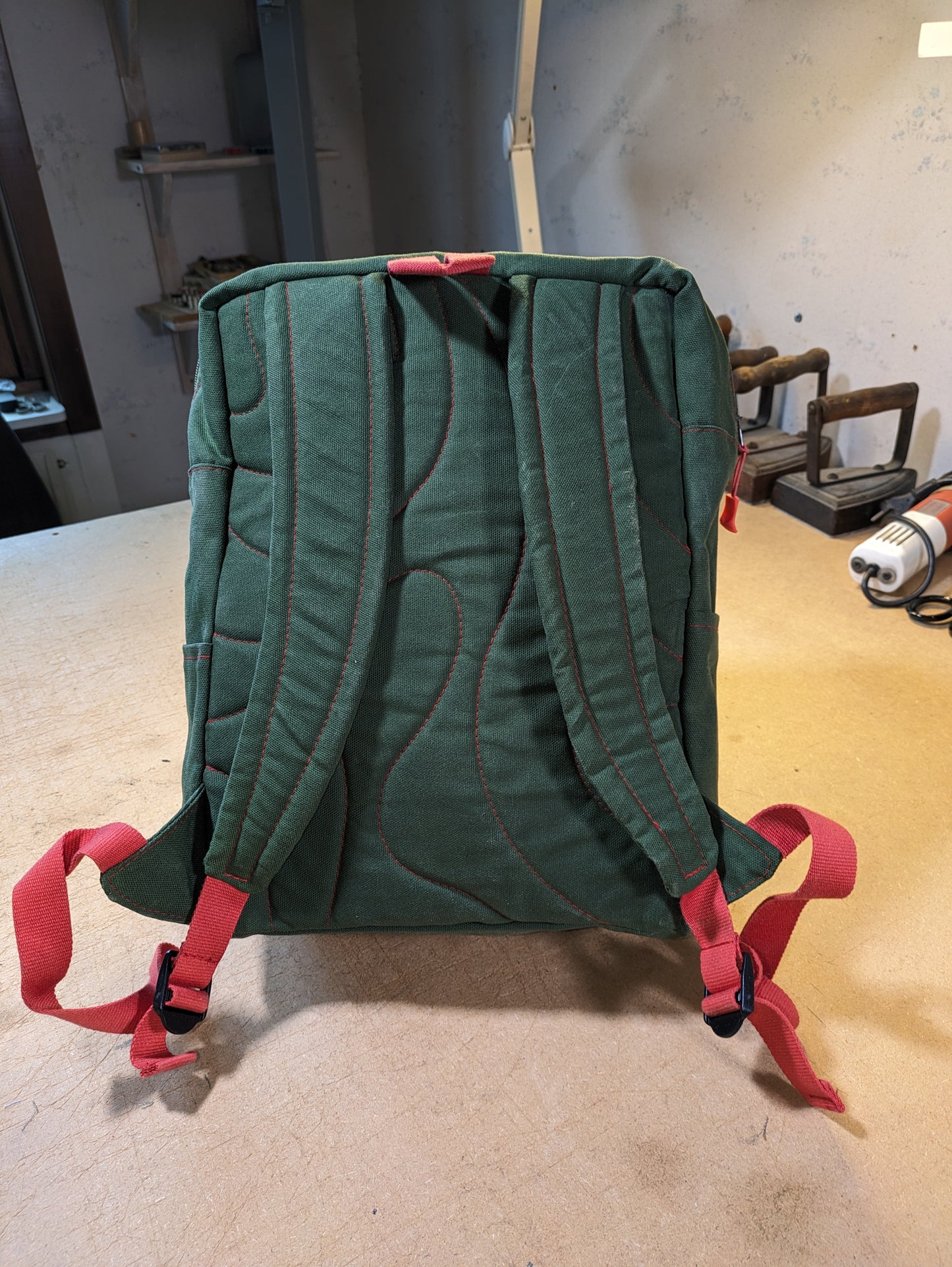 Green backpack with green zippers, red thread and straps