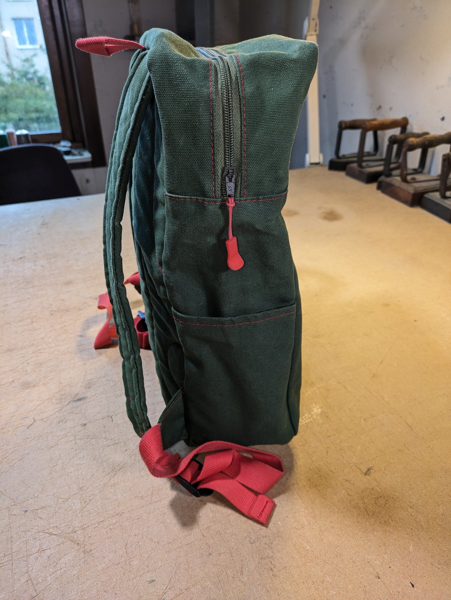 Green backpack with green zippers, red thread and straps