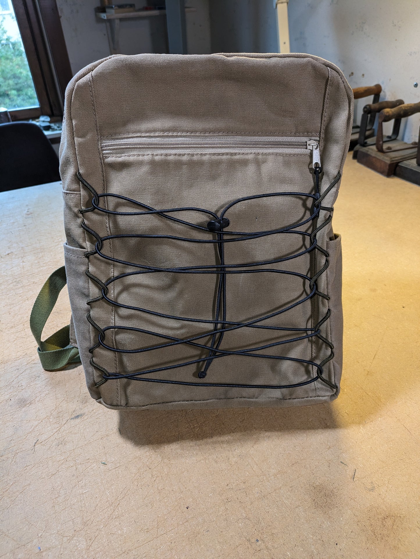 Khaki backpack with matching zippers, wire, black straps and flexcord