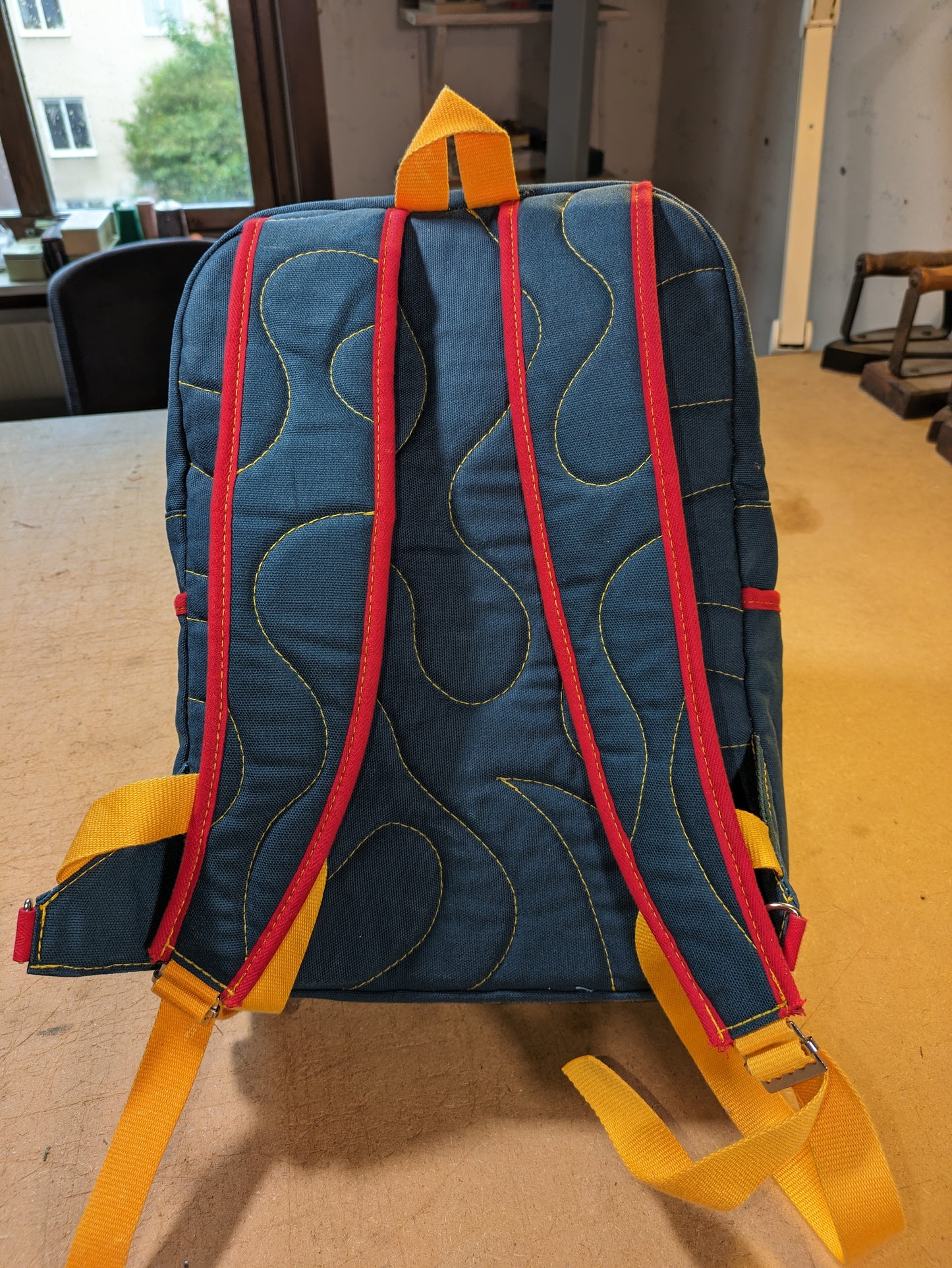 Petrol/blue backpack with red zippers, yellow thread, red and yellow straps and flexcord