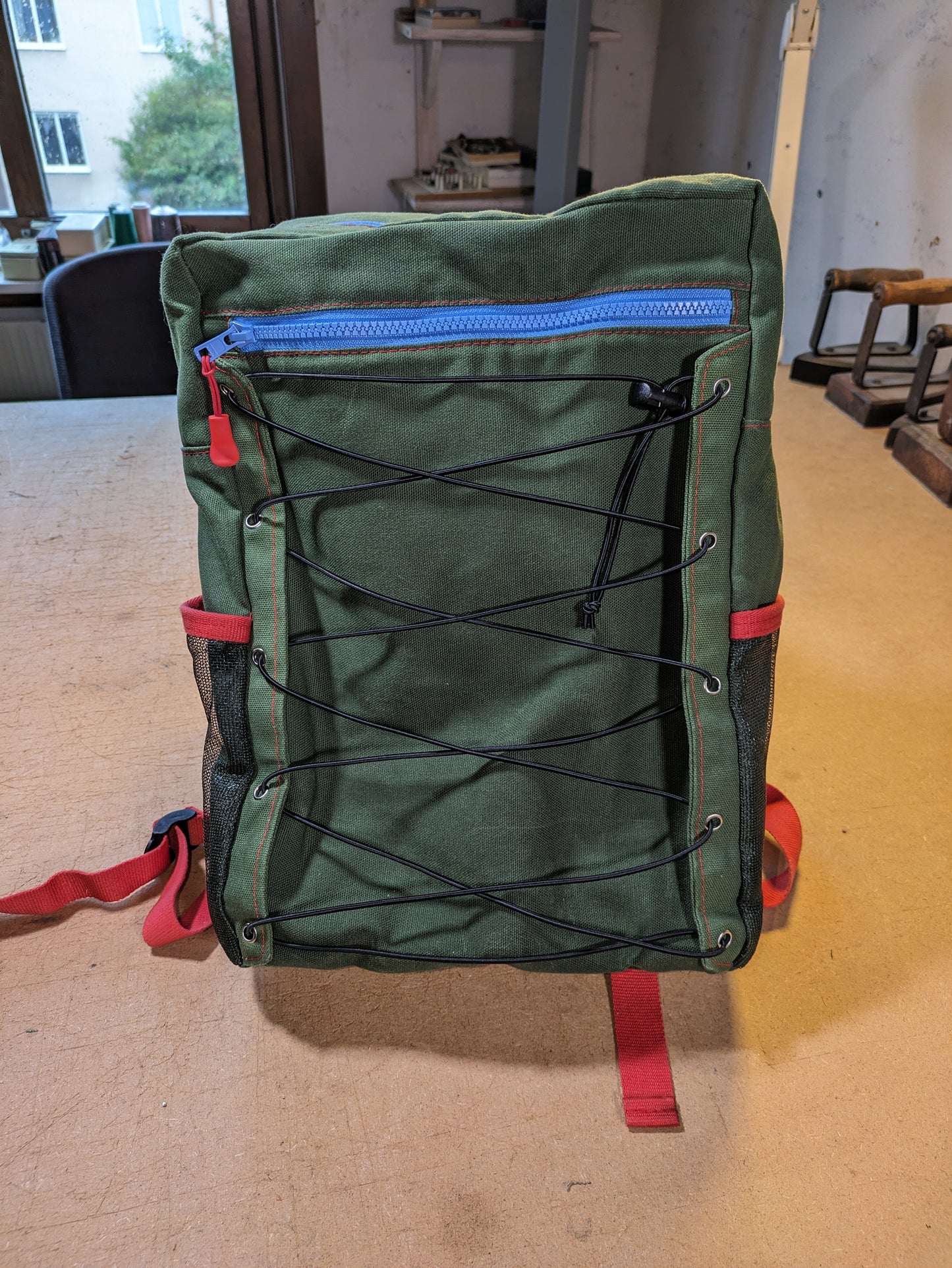 Green backpack with blue zippers, red thread, straps and flexcord