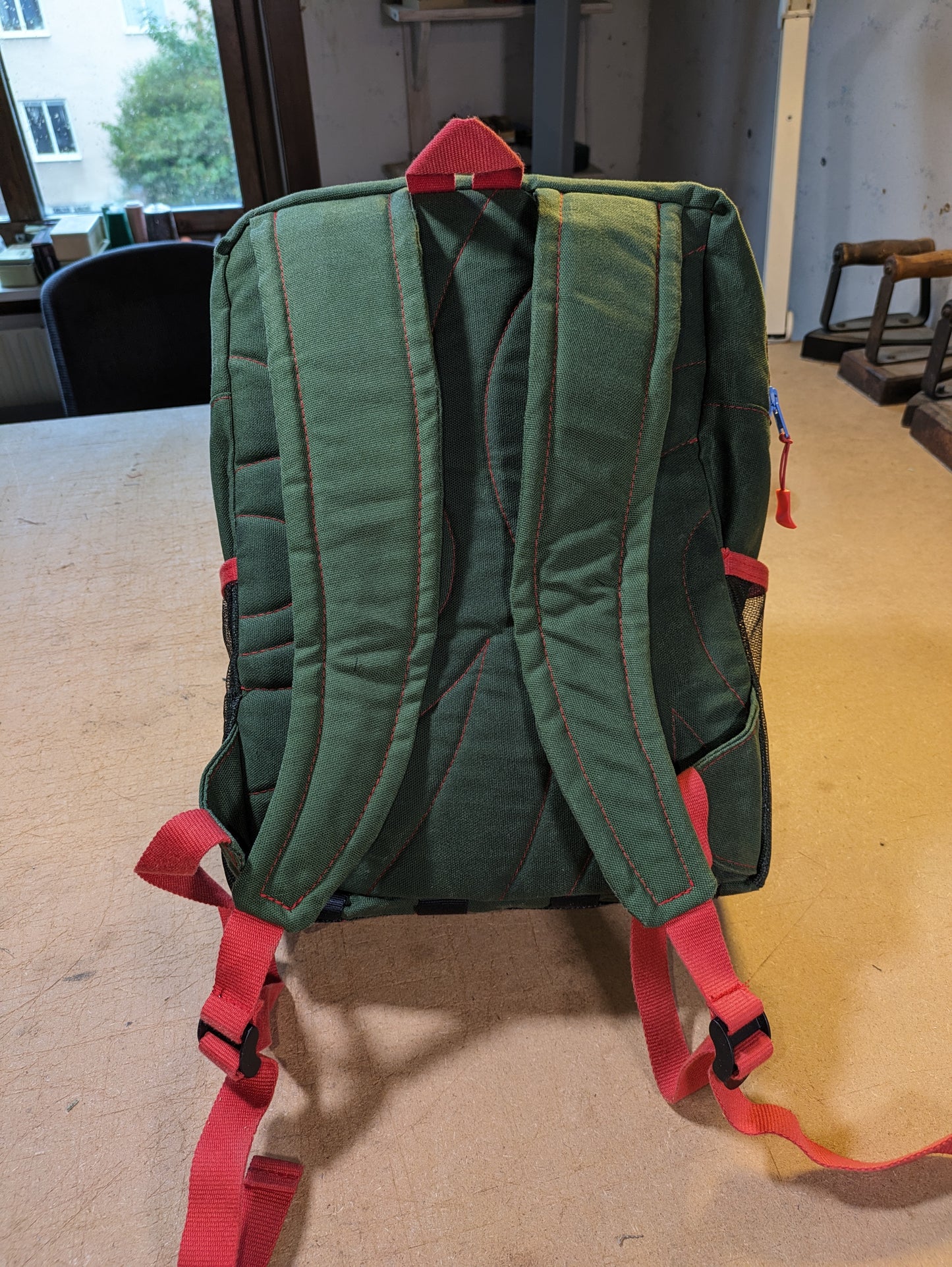 Green backpack with blue zippers, red thread, straps and flexcord