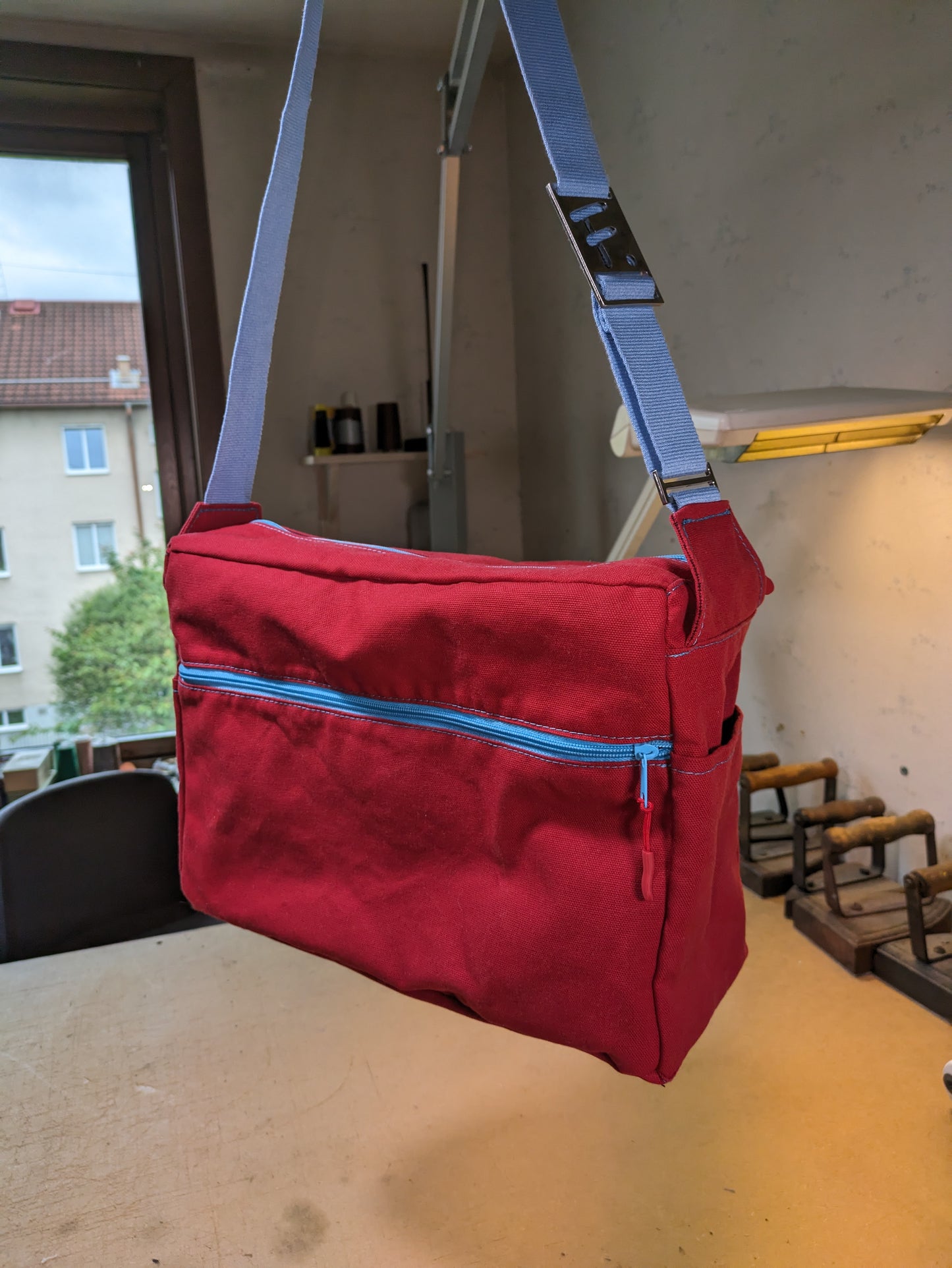 Shoulder bag in red canvas with light blue zippers and strap