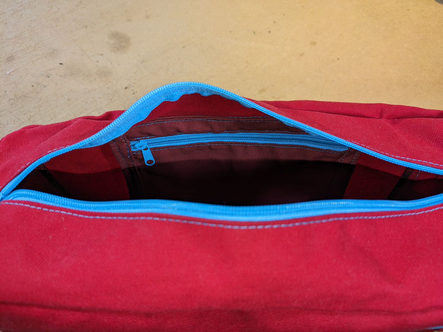 Shoulder bag in red canvas with light blue zippers and strap